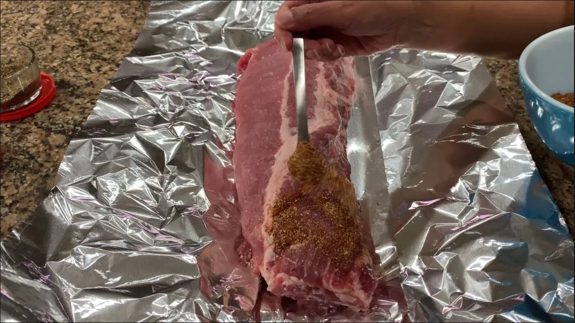 applying dry rub to cleaned baby back ribs on foil