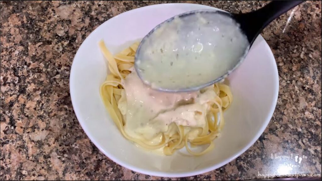 fettuccine alfredo sauce being poured on fettuccine pasta