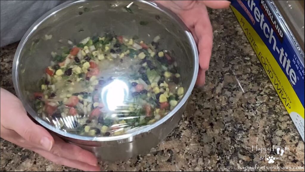 black bean salsa in a bowl being covered for storage in refrigerator