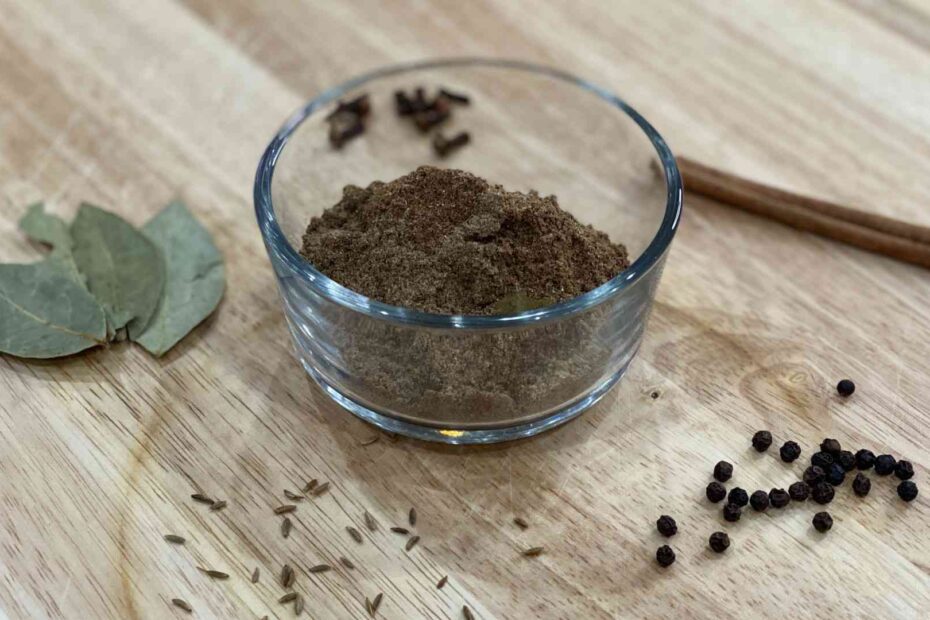 Garam Masala in a cup with ingredients used to make it on wood cutting board