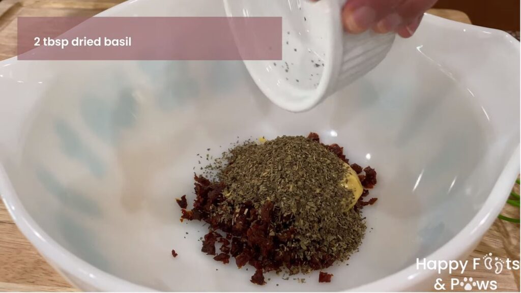Adding dried basil to sun-dried tomato vinaigrette dressing recipe in bowl