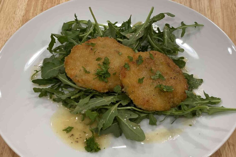 Two shrimp cakes on a plate with Beurre Blanc Sauce and arugula greens