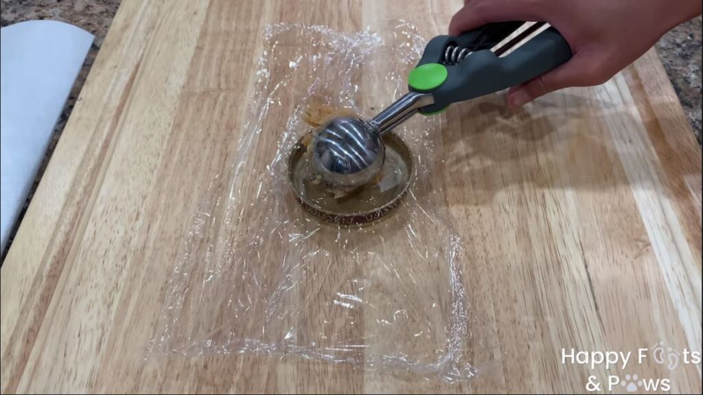 Hand with ice cream scoop placing raw shrimp cake into lid