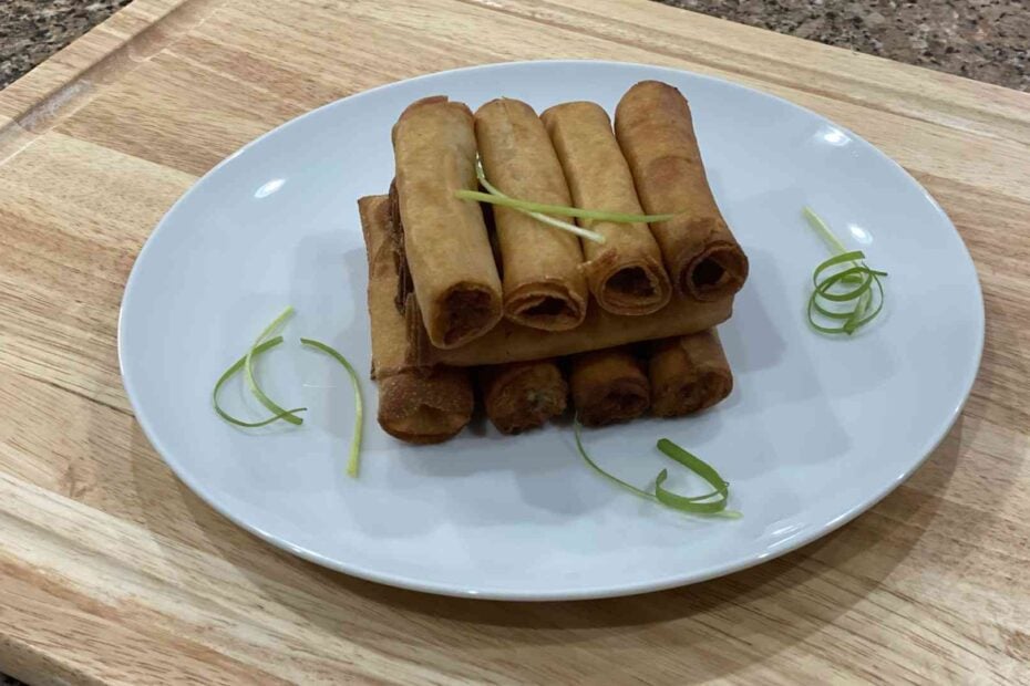 A stack of filipino lumpia shanghai on a plate with spring onions