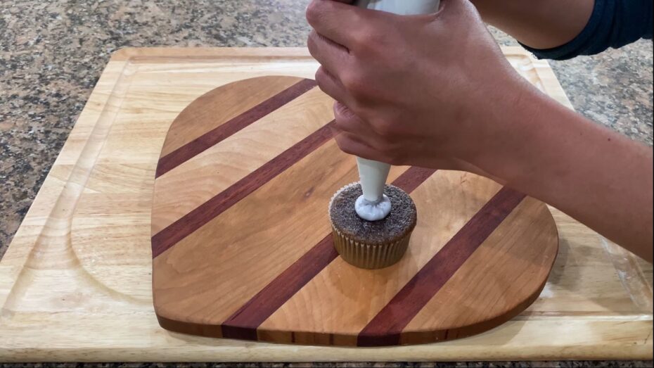 Piping the swiss meringue onto the baked ube cupcakes